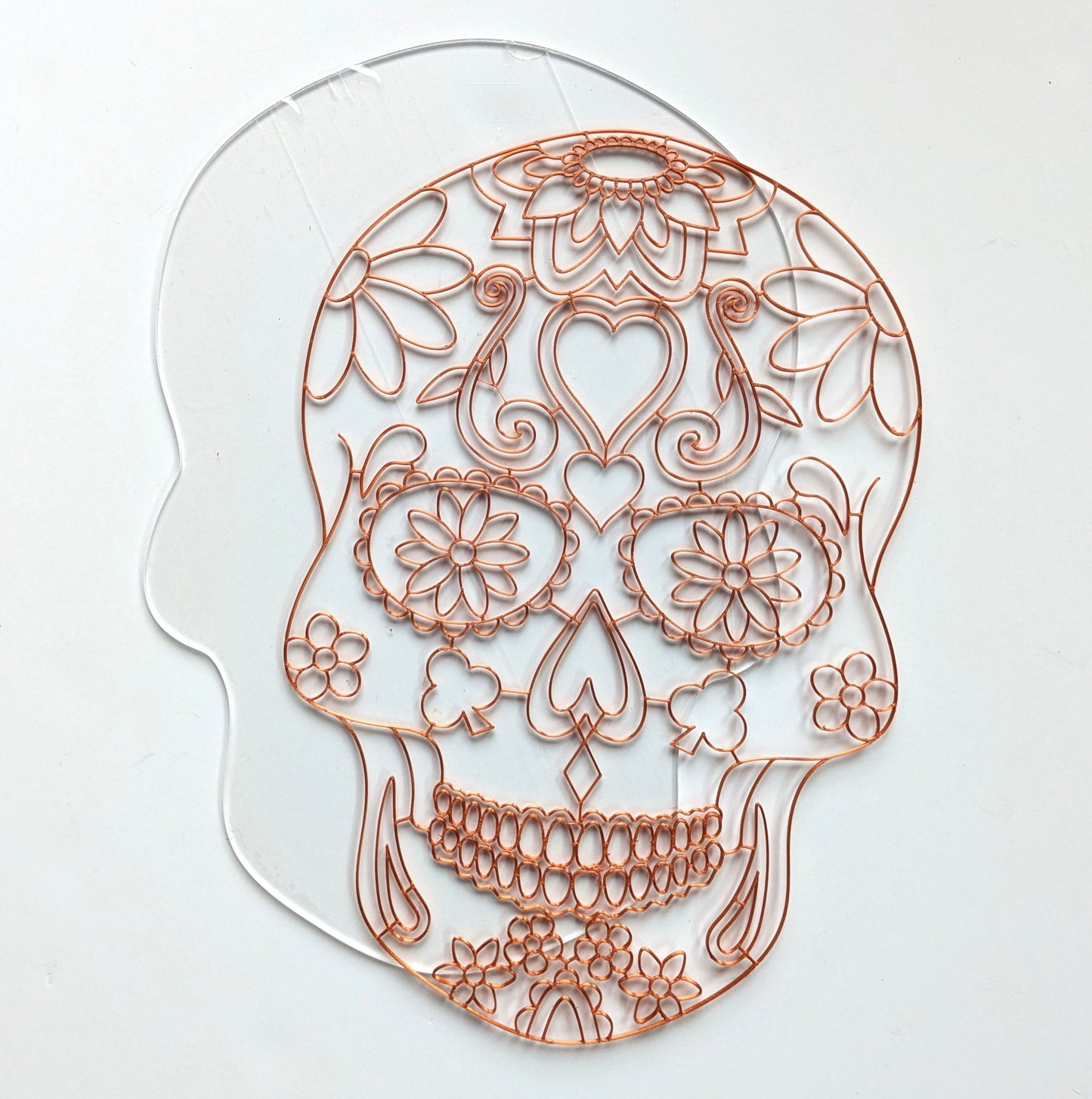 3D printed copper PLA sugar skull resin art template laid on a clear skull-shaped acrylic panel, showing floral and heart detail